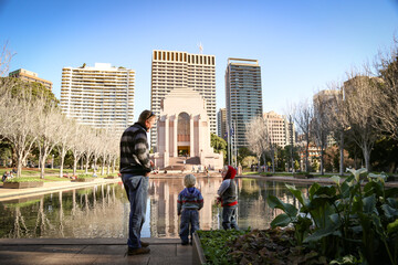Naklejka premium Father and sons enjoying quality time together standing in front of the Pool of Reflections Anzac War Memorial in Hyde Park, Sydney Australia