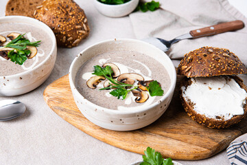 Traditional French mushroom cream soup with sour cream and parsley and rye bun on wooden board on natural linen background .