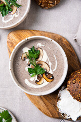 Traditional French mushroom cream soup with sour cream and parsley and rye bun on wooden board on natural linen background .