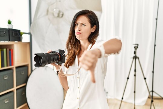 Beautiful caucasian woman working as photographer at photography studio looking unhappy and angry showing rejection and negative with thumbs down gesture. bad expression.