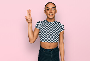 Hispanic transgender man wearing make up and long hair wearing modern clothes showing and pointing up with fingers number three while smiling confident and happy.