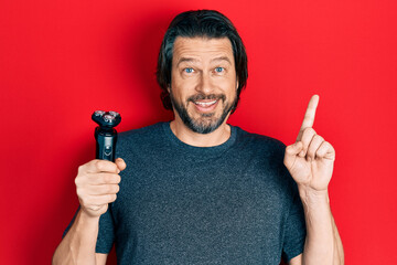 Middle age caucasian man holding electric razor machine surprised with an idea or question pointing...