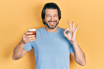 Middle age caucasian man drinking a pint of beer doing ok sign with fingers, smiling friendly gesturing excellent symbol