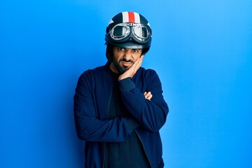 Young hispanic man holding motorcycle helmet thinking looking tired and bored with depression problems with crossed arms.