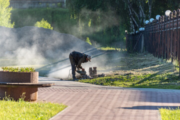 Workers lay paving stones on footpaths in a public park.