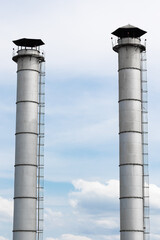 High large metal pipes of the plant gray color against the cloud light blue sky. Vertical photo of industrial metal structure against the background of clouds. High quality photo