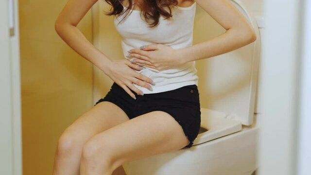 Sick young mixed race woman suffering from stomach ache sitting in toilet. She feeling so sick and painful,Healthcare concept
