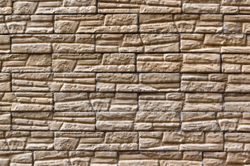 Fototapeta premium The background is the texture of a glossy soft-looking facing brick of European-looking sandy yellow. The wall is trimmed with decorative stone made of treated sandstone. High quality photo