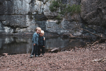 Two little boys standing together in front of rock pool on outdoor adventure