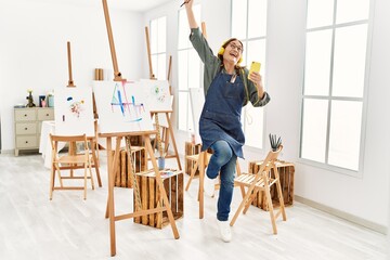 Middle age artist woman smiling happy and dancing painting at art studio.