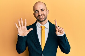 Young hispanic man wearing business suit and tie showing and pointing up with fingers number six while smiling confident and happy.