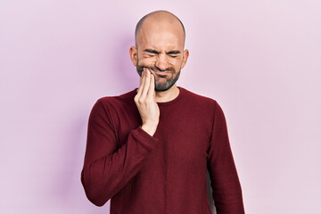 Young bald man wearing casual clothes touching mouth with hand with painful expression because of toothache or dental illness on teeth. dentist