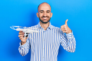 Naklejka premium Young bald man holding drone smiling happy and positive, thumb up doing excellent and approval sign