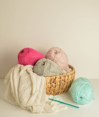 Fototapeta na wymiar soft colored woolen balls in basket with crochet hook and a white woolen blanket