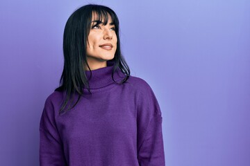 Young brunette woman with bangs wearing turtleneck sweater looking away to side with smile on face, natural expression. laughing confident.