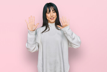 Young brunette woman with bangs wearing casual turtleneck sweater showing and pointing up with fingers number ten while smiling confident and happy.