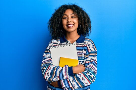 Beautiful african american woman with afro hair holding books smiling with a happy and cool smile on face. showing teeth.