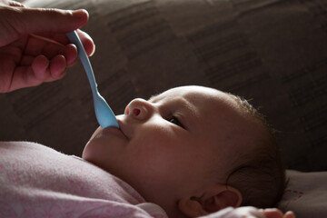 Parent giving water to small child with spoon, close up
