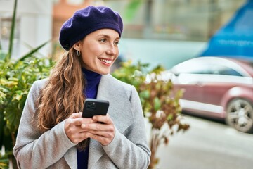 Young blonde woman smiling happy using smartphone at the city.