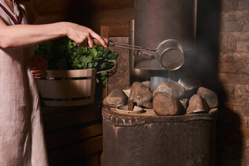 woman in a bath pours water on hot stones on the stove