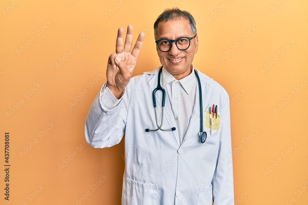 Sticker middle age indian man wearing doctor coat and stethoscope showing and pointing up with fingers numbe