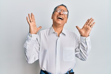 Fototapeta premium Middle age indian man wearing casual clothes and glasses celebrating mad and crazy for success with arms raised and closed eyes screaming excited. winner concept