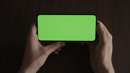 Man using phone with green screen on black wwalnut table