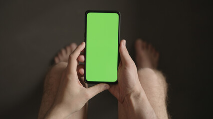 Man using phone with green screen while sitting with naked legs