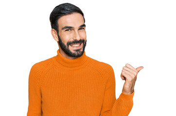 Young hispanic man wearing casual clothes smiling with happy face looking and pointing to the side with thumb up.