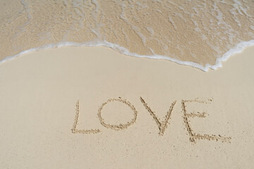 The text LOVE on the sand of a tropical beach, in the background the waves of the Caribbean sea in Mexico 