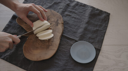 Man slicing mozzarella on olive wood board for sandwich