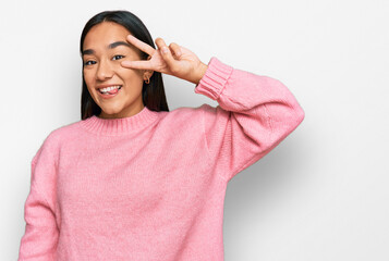 Young asian woman wearing casual winter sweater doing peace symbol with fingers over face, smiling cheerful showing victory