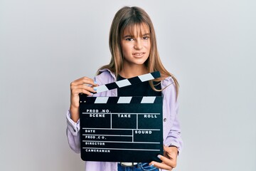Teenager caucasian girl holding video film clapboard clueless and confused expression. doubt...