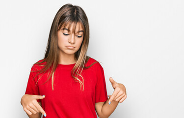 Teenager caucasian girl wearing casual red t shirt pointing down looking sad and upset, indicating direction with fingers, unhappy and depressed.