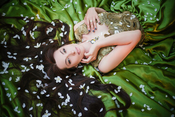 A beautiful young woman in a green dress lies on a train among the white petals of an apple tree.