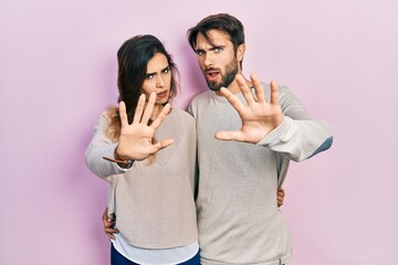 Young hispanic couple wearing casual clothes doing stop gesture with hands palms, angry and frustration expression