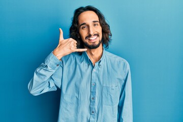 Young hispanic man wearing casual clothes smiling doing phone gesture with hand and fingers like talking on the telephone. communicating concepts.