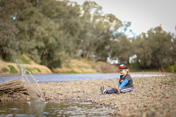 Little boy sitting on edge of riverbank throwing rocks to make splash
