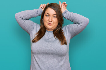 Fototapeta premium Beautiful brunette plus size woman wearing casual clothes doing funny gesture with finger over head as bull horns