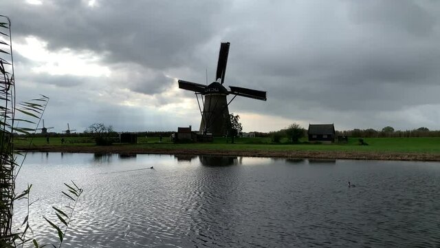 Old Dutch Kinderdijk windmill with moving blades next to the canal. Kinderdijk, Netherlands.