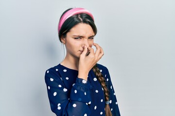 Young brunette girl wearing elegant look smelling something stinky and disgusting, intolerable smell, holding breath with fingers on nose. bad smell