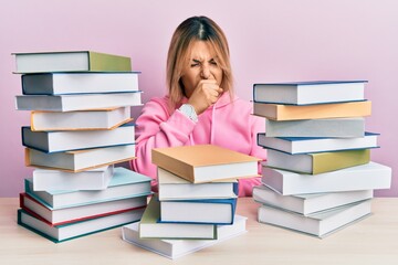 Young caucasian woman sitting on the table with books feeling unwell and coughing as symptom for cold or bronchitis. health care concept.