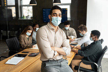 Young arab businessman in mask sitting on desk and posing