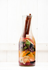 Summer detox and refreshing drink lemonade with fresh fruits, berries and herbs in glass bottle on white wooden background