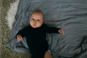 baby lies in a black bodysuit on his back on the bed