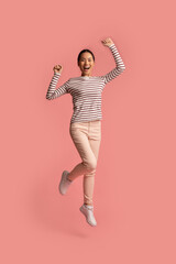 Euphoric Young Asian Woman Jumping With Raised Hands Over Pink Background