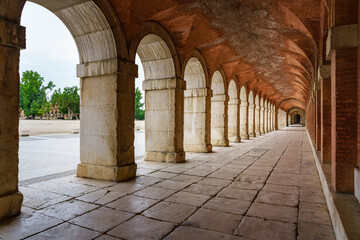 Obraz premium Large symmetrical exterior corridor with arches and columns in the old royal palace of Aranjuez.