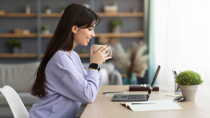 Smiling woman watching video on computer, drinking coffee