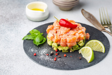 Delicious avocado and raw salmon salad, tartare, served on a black plate with lime, light background