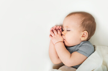 Toddler sleeps with finger in mouth on bed close-up. Healthy baby sleep concept and copy space.
